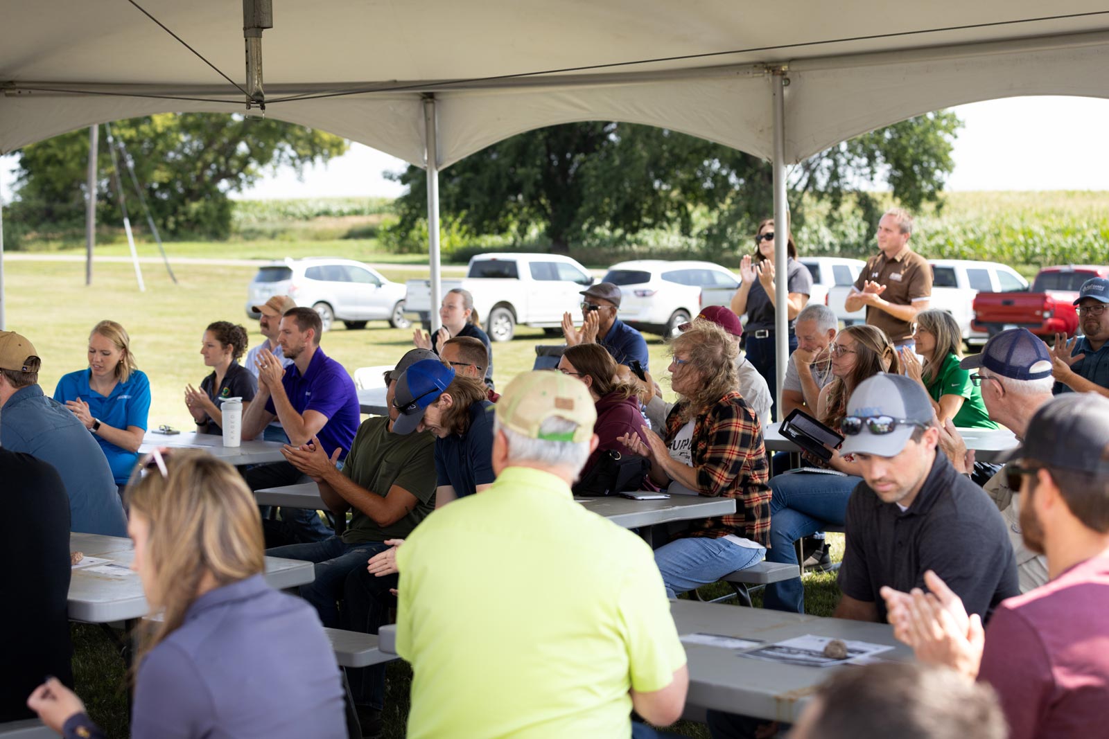 A crowd of people sitting at picnic tables under a canopy