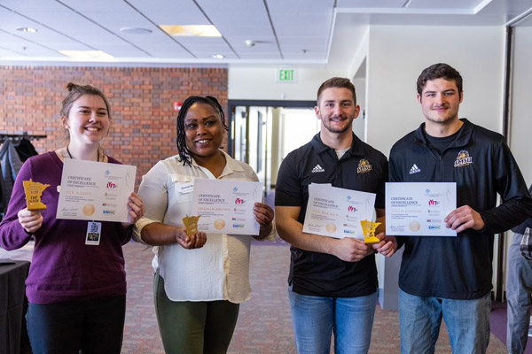 Competition picture of 4 SMSU Students holding Certificate of Excellence Awards.