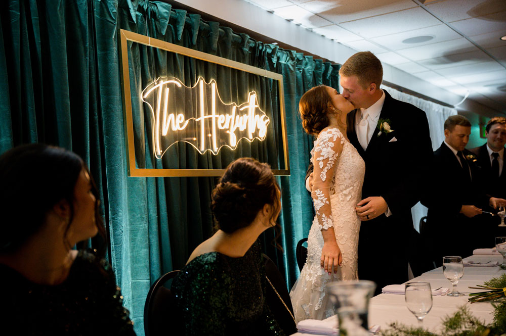 bride and groom kiss in front of velvet green backdrop