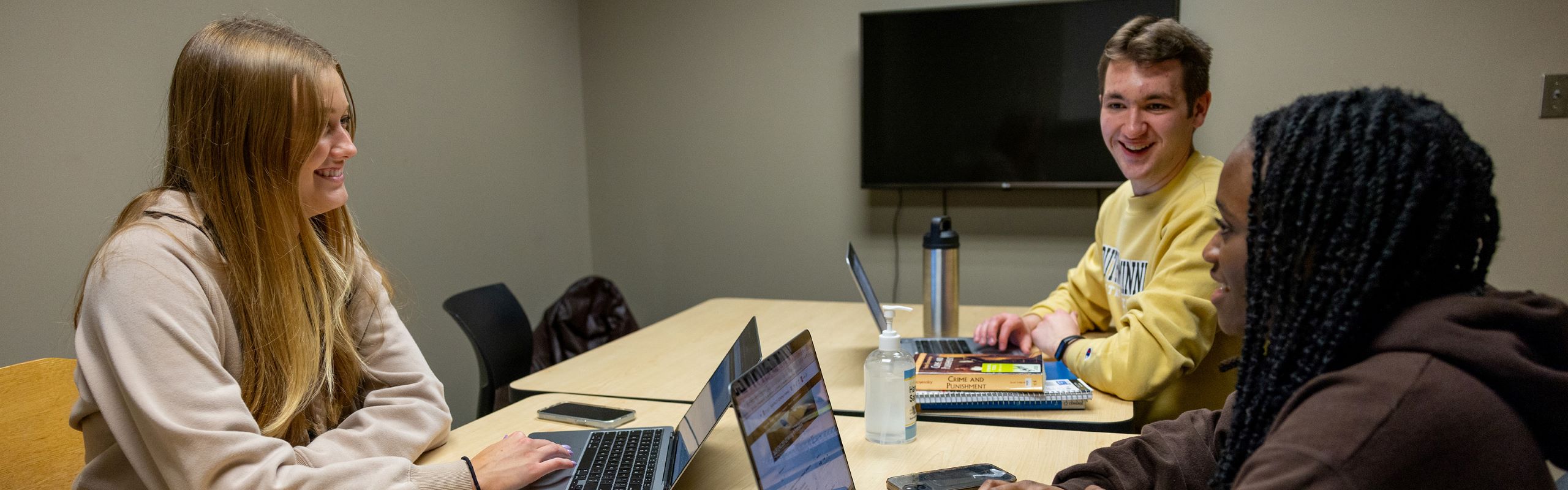 A picture of three students using their laptops in a group study room. 